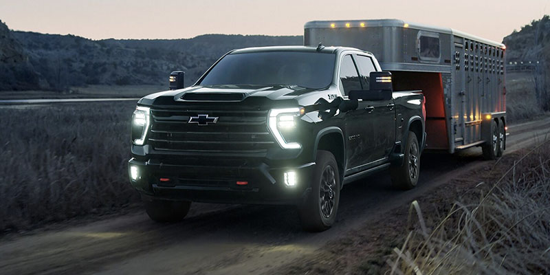 Chevrolet Silverado 2500 HD towing a trailer on a rugged road at dusk.