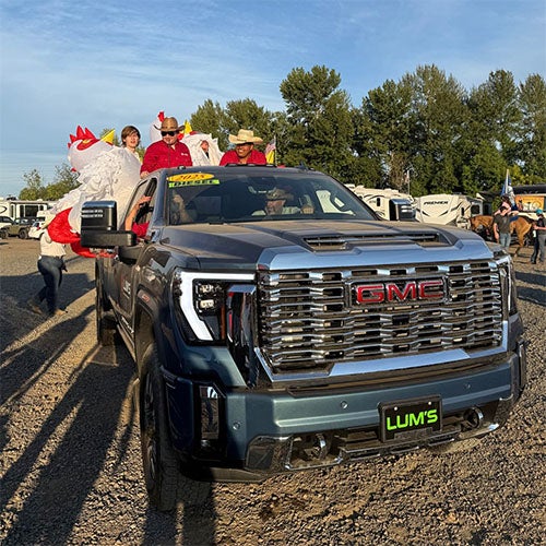 A GMC pickup truck with several people in it. One person in the truck bed is wearing a large chicken costume.