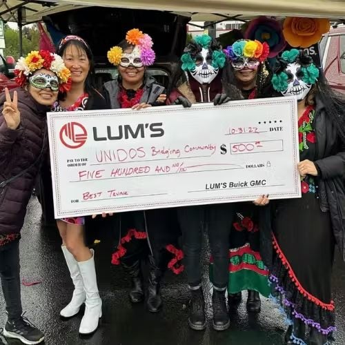 Six people in Day of the Dead costumes hold a giant check for $500 to Unidos Bridging Community for 'Best Trunk'.
