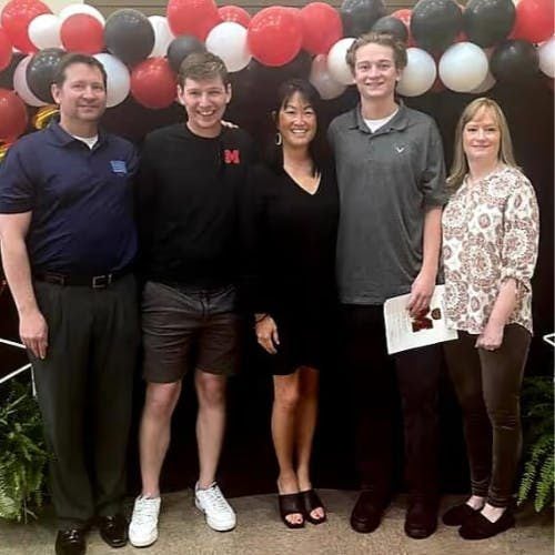 Five people, three men and two women, pose in front of red, white, and black balloons.