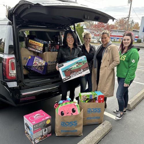 Four smiling women next to an SUV trunk filled with donated items. Two Ross bags are on the ground.