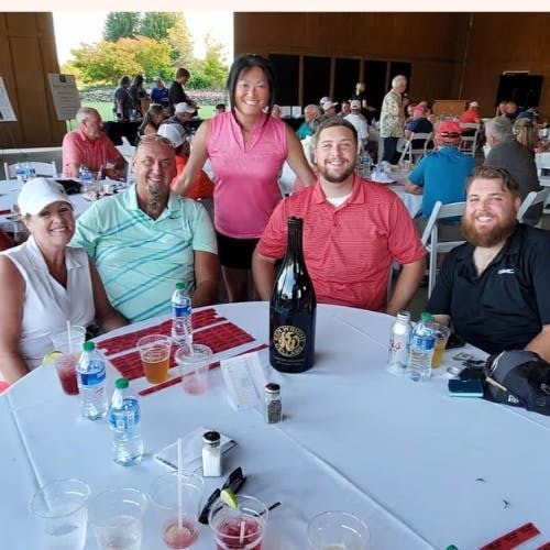Five people smiling at a table with drinks and a wine bottle.